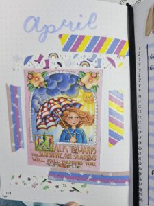 Journal page with April written in brush pen at the tops and a picture of a girl holding an umbrella in the center surrounded by coordinating washi tape